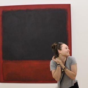 A student smiling in front of a large red and black painting