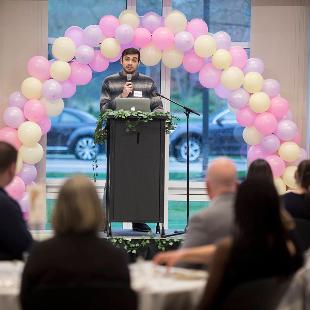 A Hope Forward student speaking into a microphone at a podium with an arch of balloons behind him