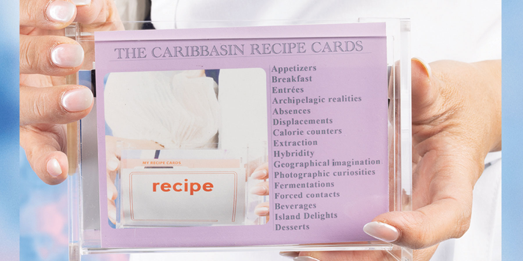 Photograph of hands holding the title card of a series called The CaribBasin Recipe Cards. 