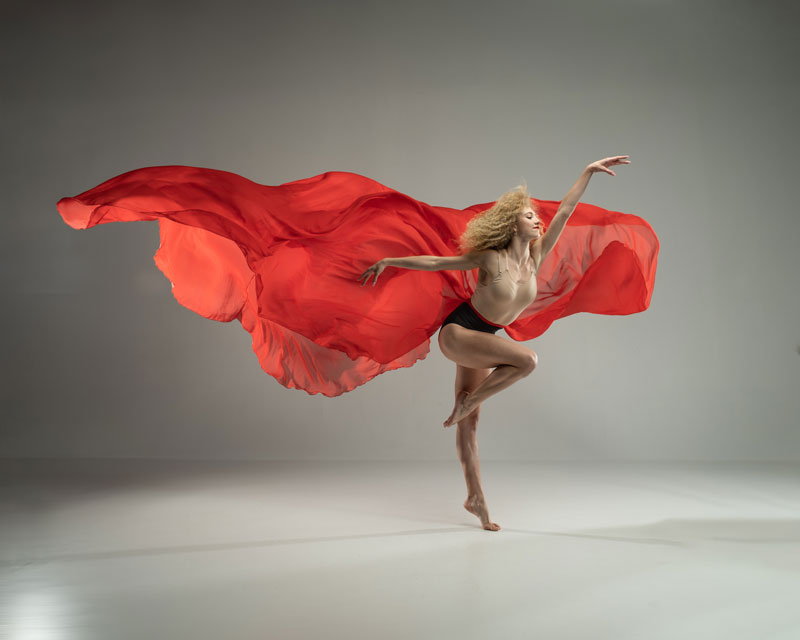 A female dancer with a billowy red costume in front of a gray background